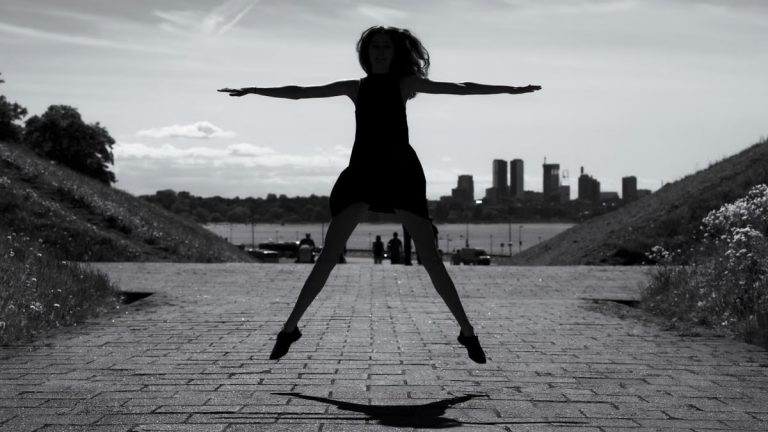 A dynamic black and white silhouette of a woman jumping with arms outstretched in Tallinn, Estonia.