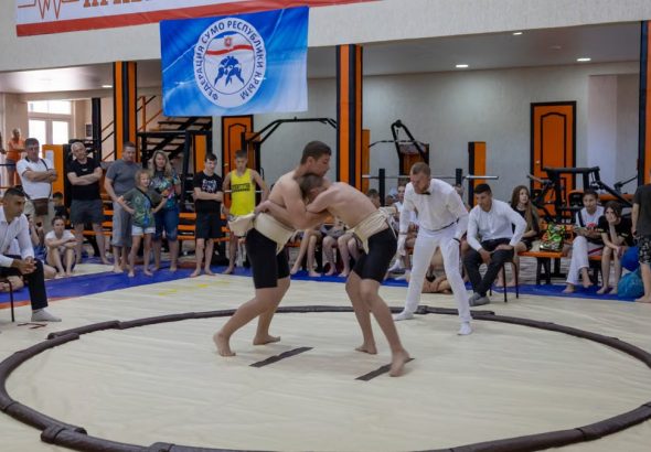 Young athletes engaged in sumo wrestling in a gym with spectators and a referee observing.